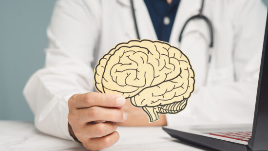 Doctor holding a brain illustration cutout, symbolizing neurology and mental health concepts.